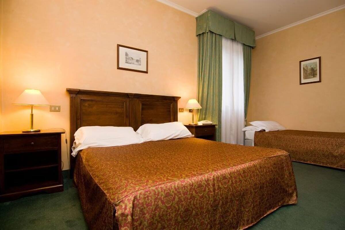A hotel room with a large bed, two bedside tables, a nightstand, and a window with curtains.