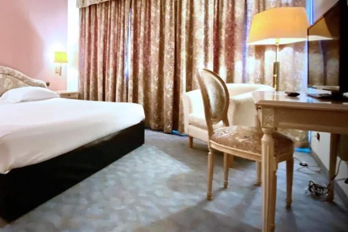 Una habitación de hotel con una cama grande, un escritorio, una silla y dos lámparas.