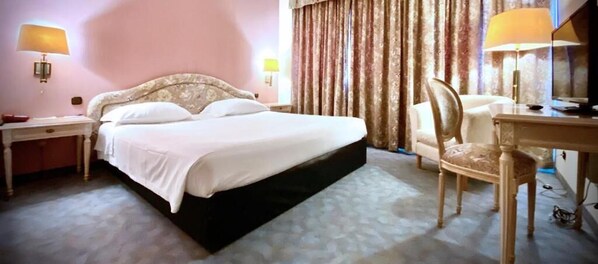 A hotel room with a large bed, a desk, a chair, and two lamps.