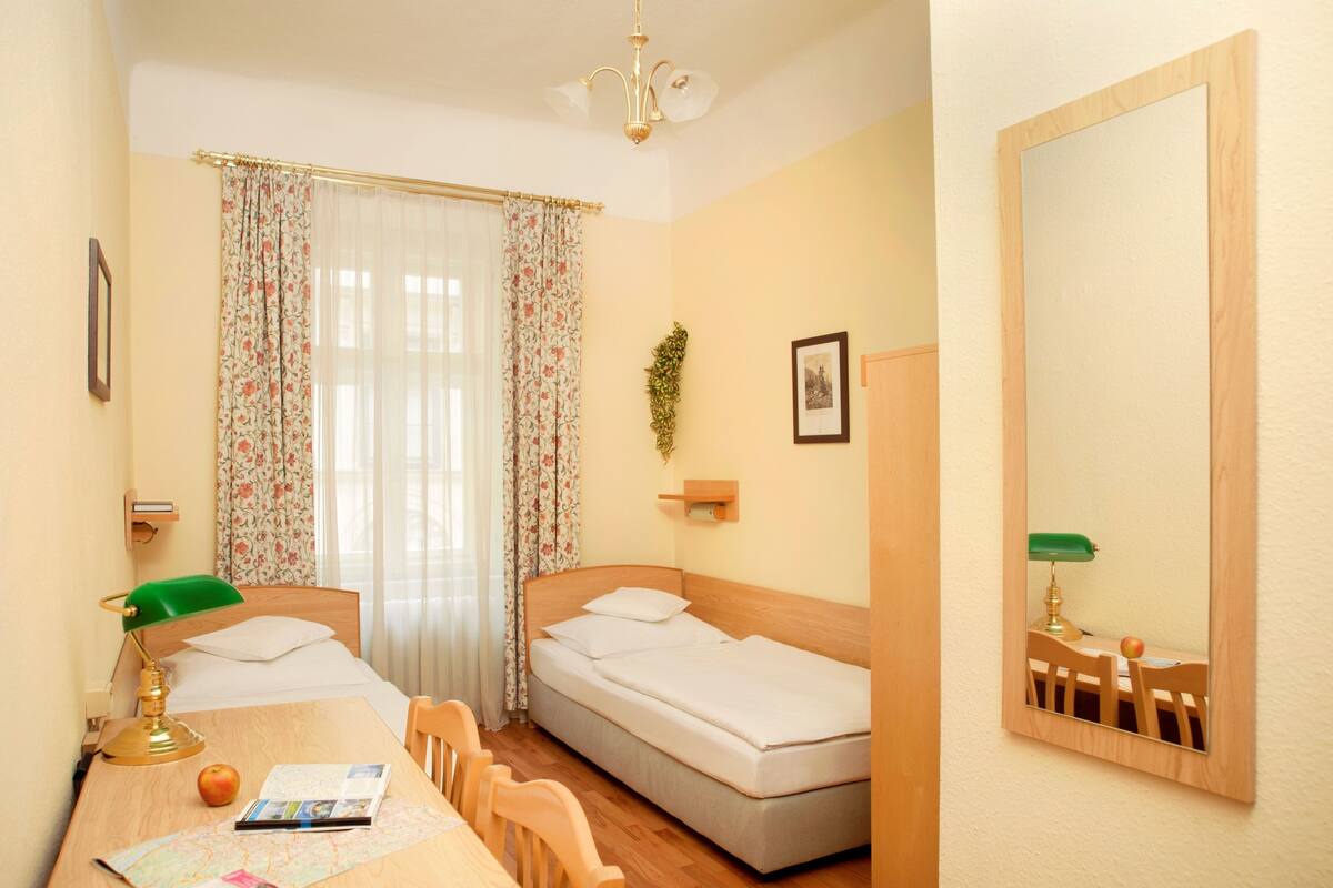 Une petite pièce bien éclairée, avec un lit, un bureau et une chaise, une carte et un miroir.