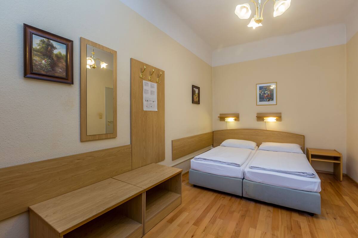 Une chambre à coucher avec un lit double, un banc en bois, un miroir et deux lampes fixées au mur.