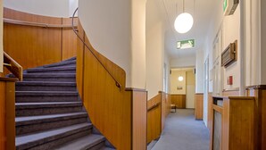 A carpeted staircase with wooden handrails and walls, leading to a room with a door and a light fixture. - Hotel Graf Stadion (Vienna)
