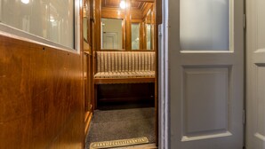 A narrow hallway with wooden walls and a bench with a patterned cushion. A door with a sign reading "HANNS FUGLISTER WIEN" is visible. - Hotel Graf Stadion (Vienna)