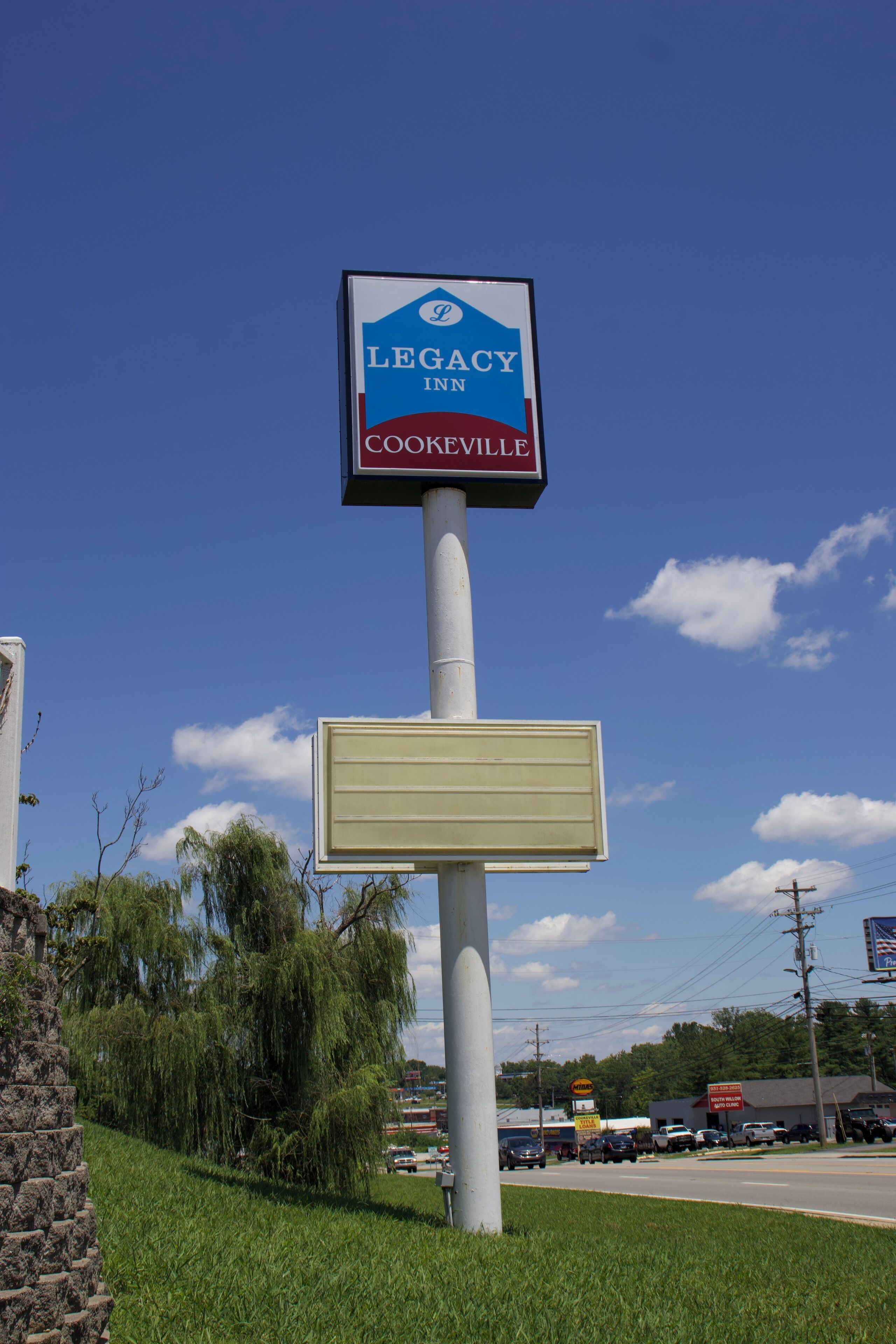Une enseigne indiquant l’emplacement du Legacy Inn à Cookeville, offrant une vue dégagée sur les environs, notamment une route, des voitures garées et un bâtiment en arrière-plan.