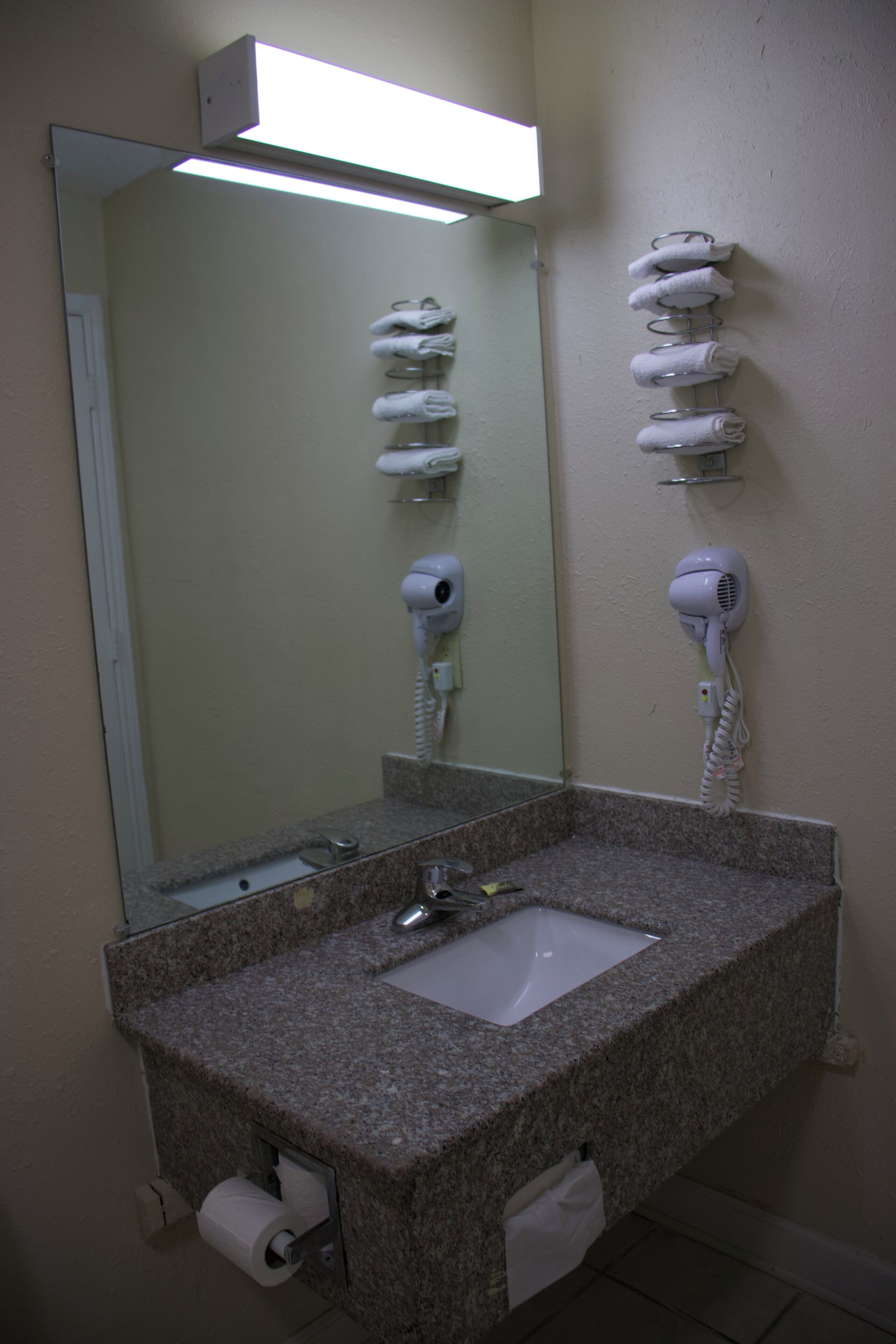 A bathroom with a granite countertop sink, a mirror, and two hair dryers mounted on the wall.