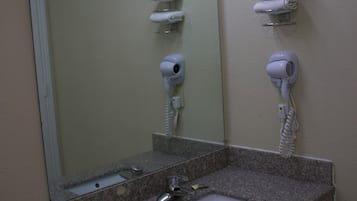 A bathroom with a granite countertop sink, a mirror, and two hair dryers mounted on the wall.