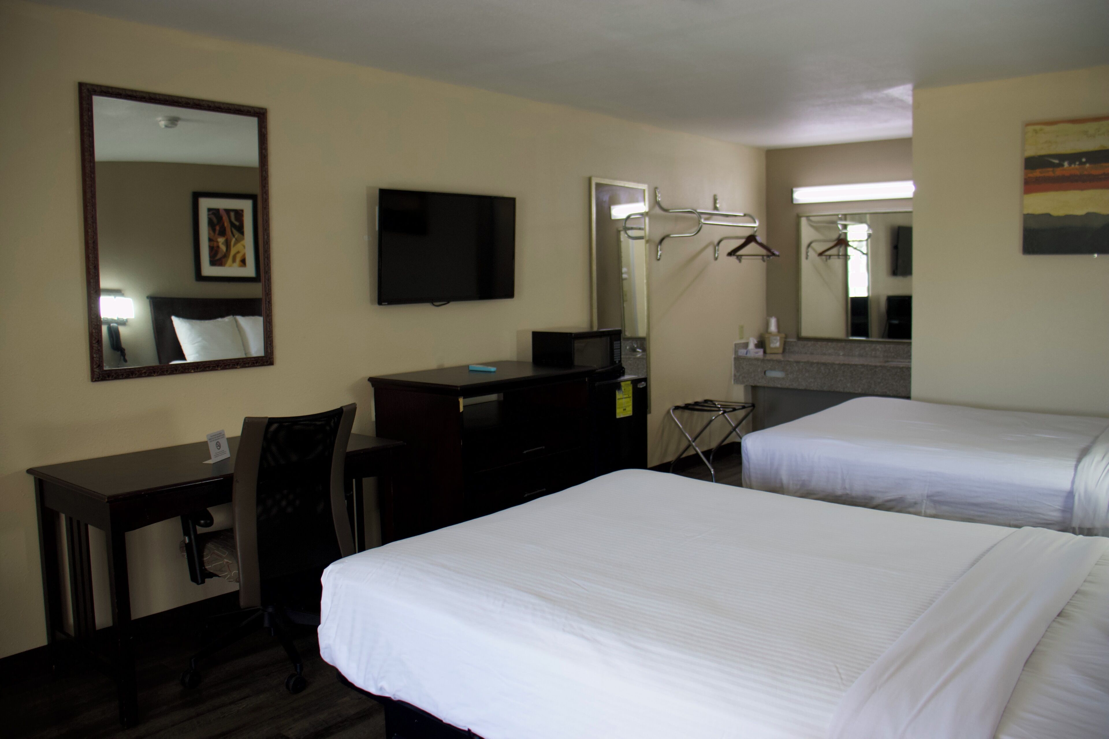 Une chambre d’hôtel avec deux lits, un bureau, une chaise, une télévision, un miroir et un four à micro-ondes.