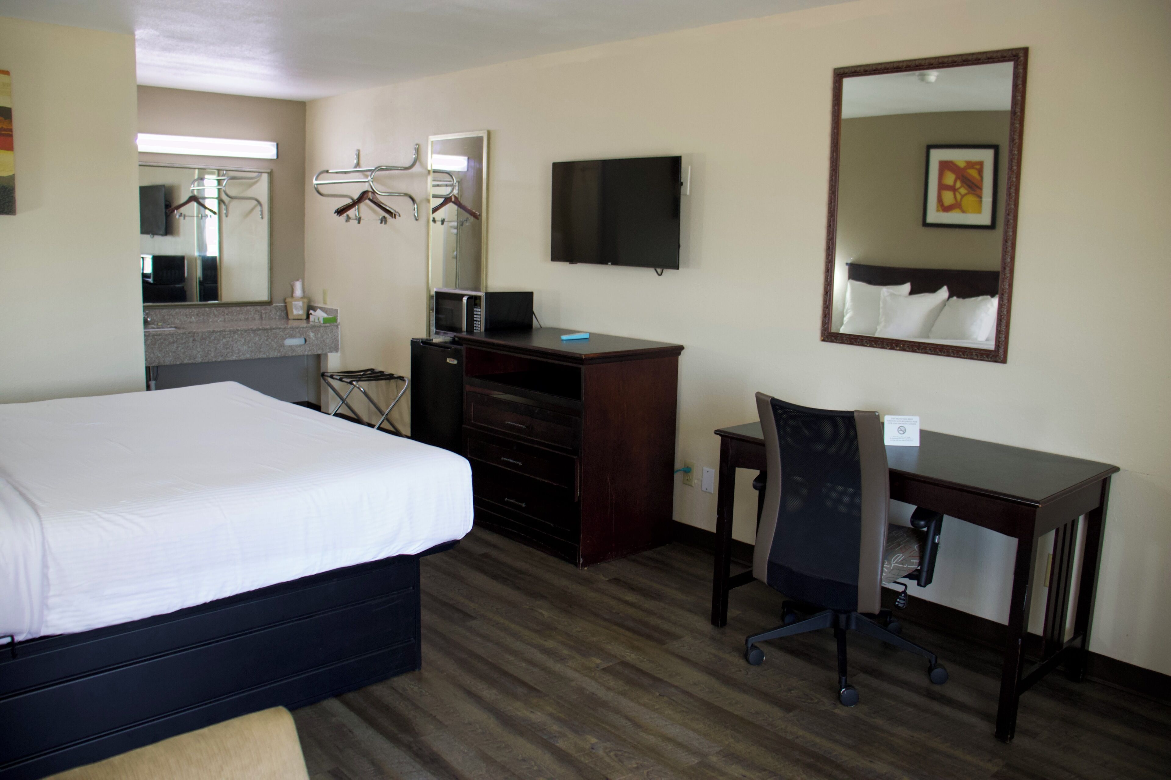 Habitación de hotel con cama, escritorio con silla, televisor de pantalla plana, espejo y microondas.