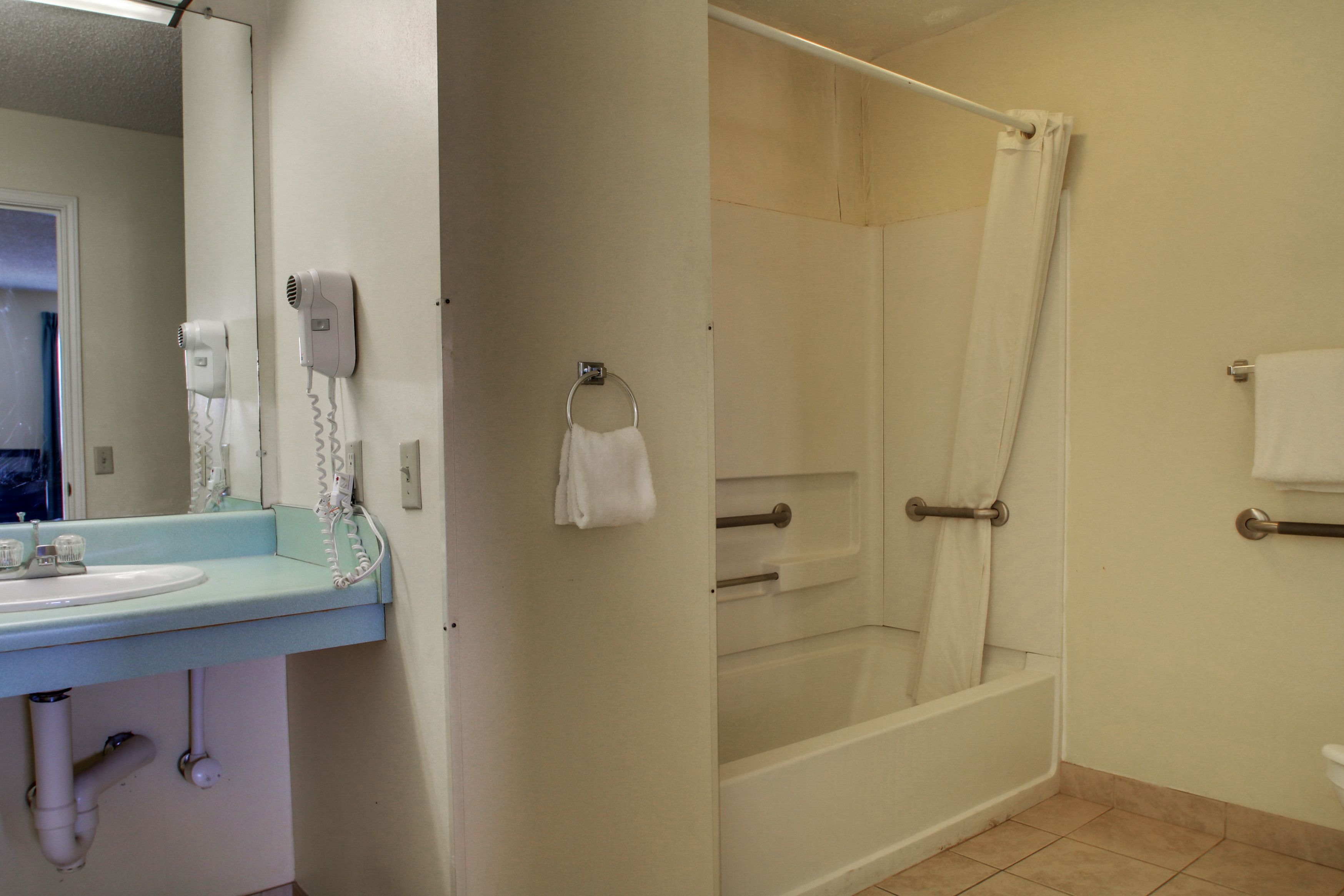 A bathroom with a sink, mirror, hair dryer, and shower.