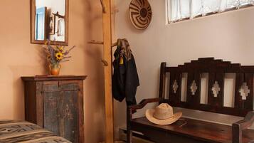 Una habitación rústica con una cama de madera, una silla de madera con un sombrero, un espejo y una pared decorada con un plato.