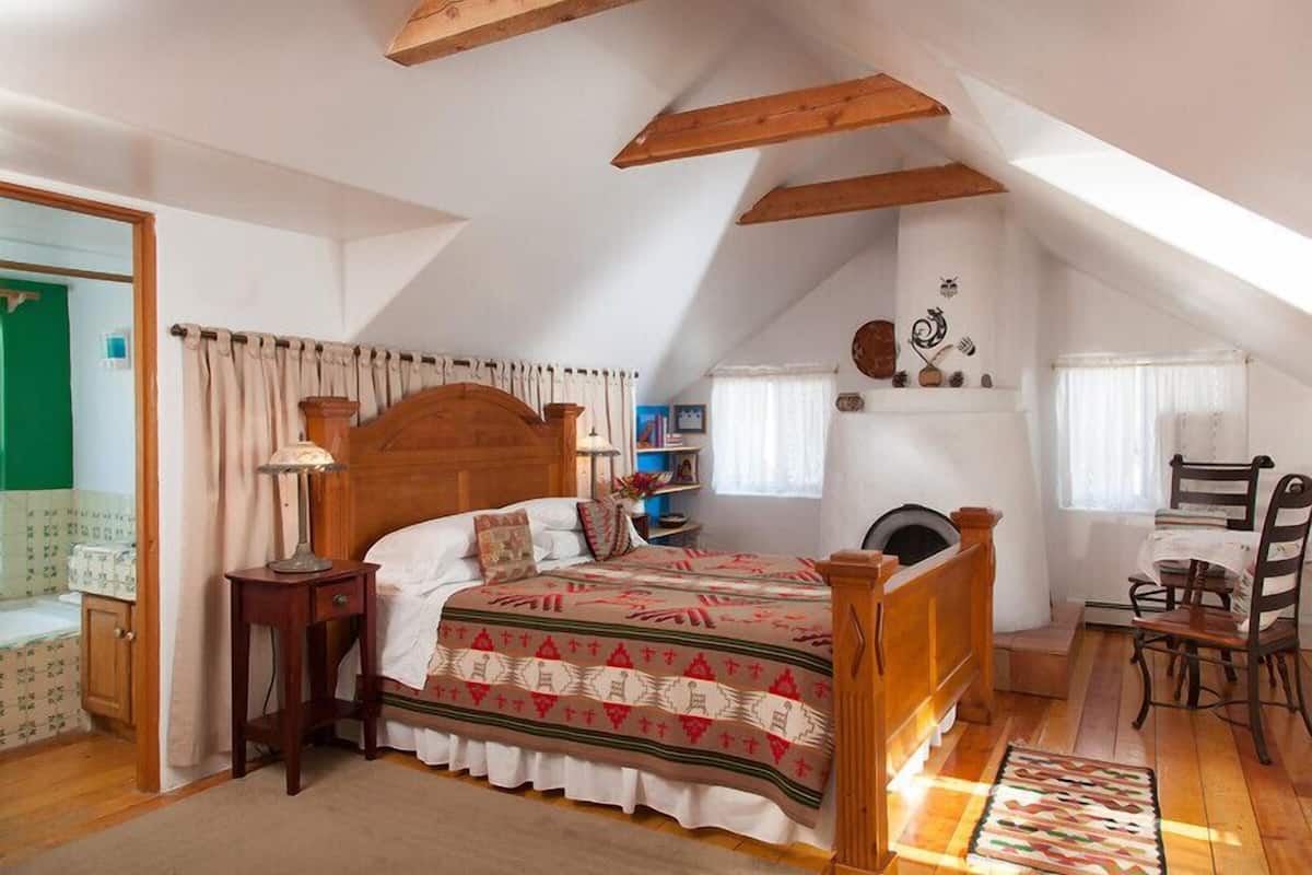 Une chambre à coucher avec un lit en bois, une table de chevet, une chaise, une fenêtre avec des rideaux et une étagère ornée d’objets décoratifs.