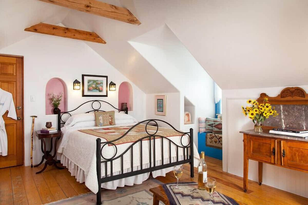 Une chambre à coucher avec un lit, des poutres en bois, une commode et un vase rempli de tournesols.