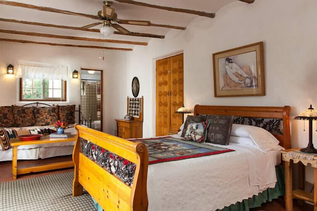Une chambre avec un lit en bois, un banc en bois, une table de chevet en bois, une armoire en bois, une porte en bois et un ventilateur de plafond.