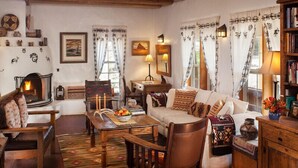 A cozy living room with a fireplace, wooden furniture, and decorative pillows. - Casa Escondida Bed & Breakfast (Chimayo)