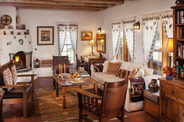 A cozy living room with a fireplace, wooden furniture, and decorative pillows. - Casa Escondida Bed & Breakfast (Chimayo)