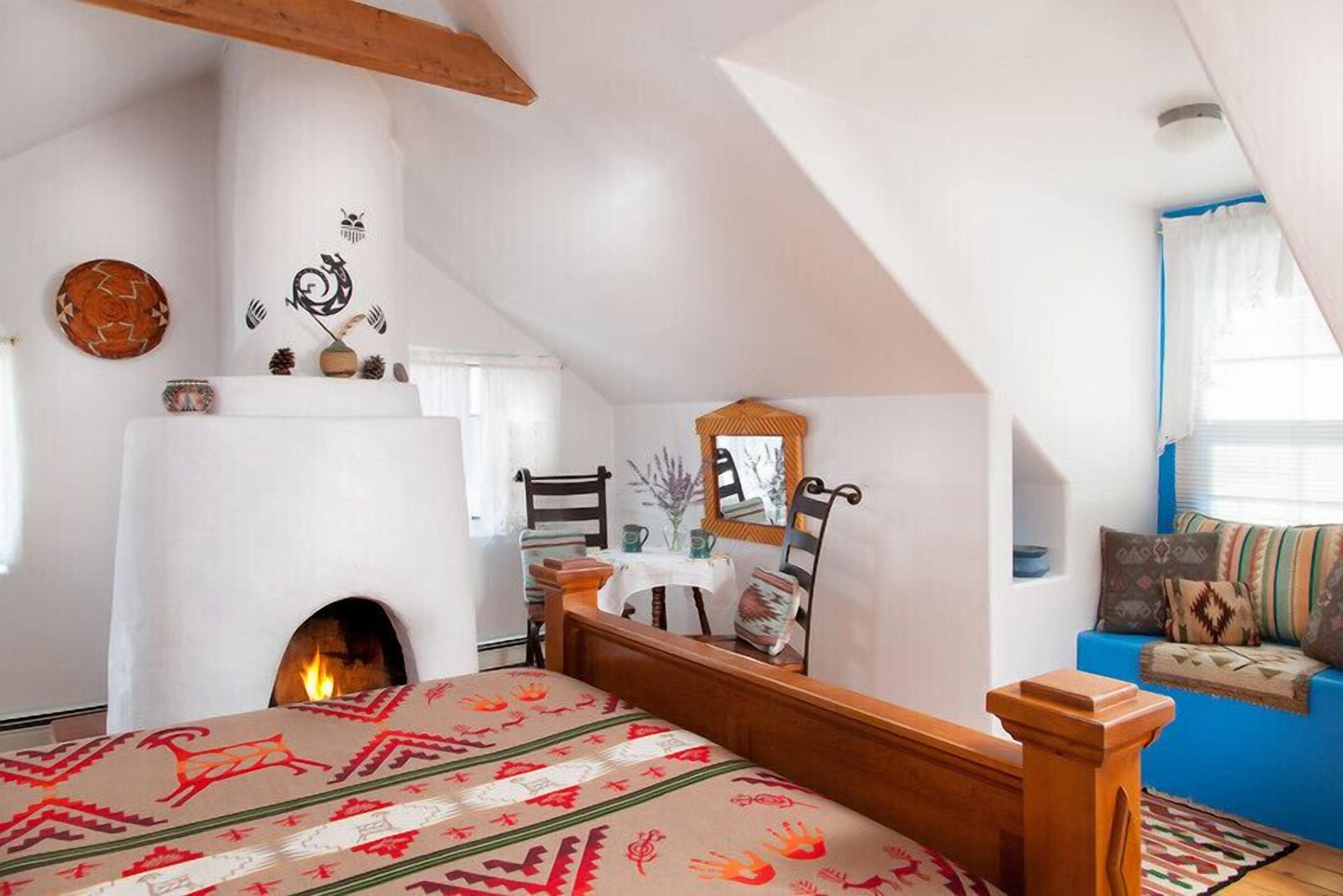 Un dormitorio con chimenea, una cama con colcha estampada, un sofá azul y una silla de madera.