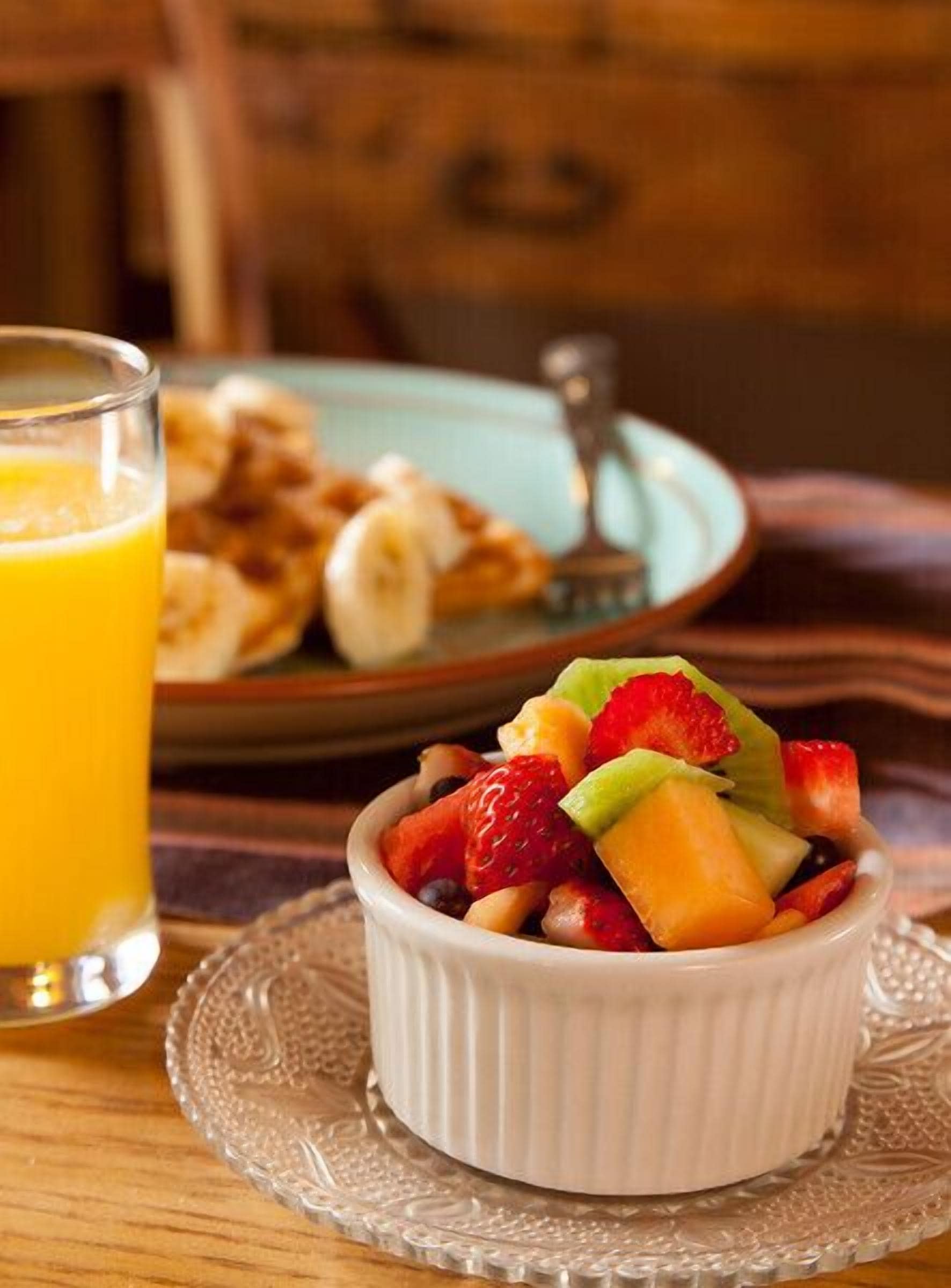Un desayuno con ensalada de frutas, un vaso de zumo de naranja y una fuente de tortitas.