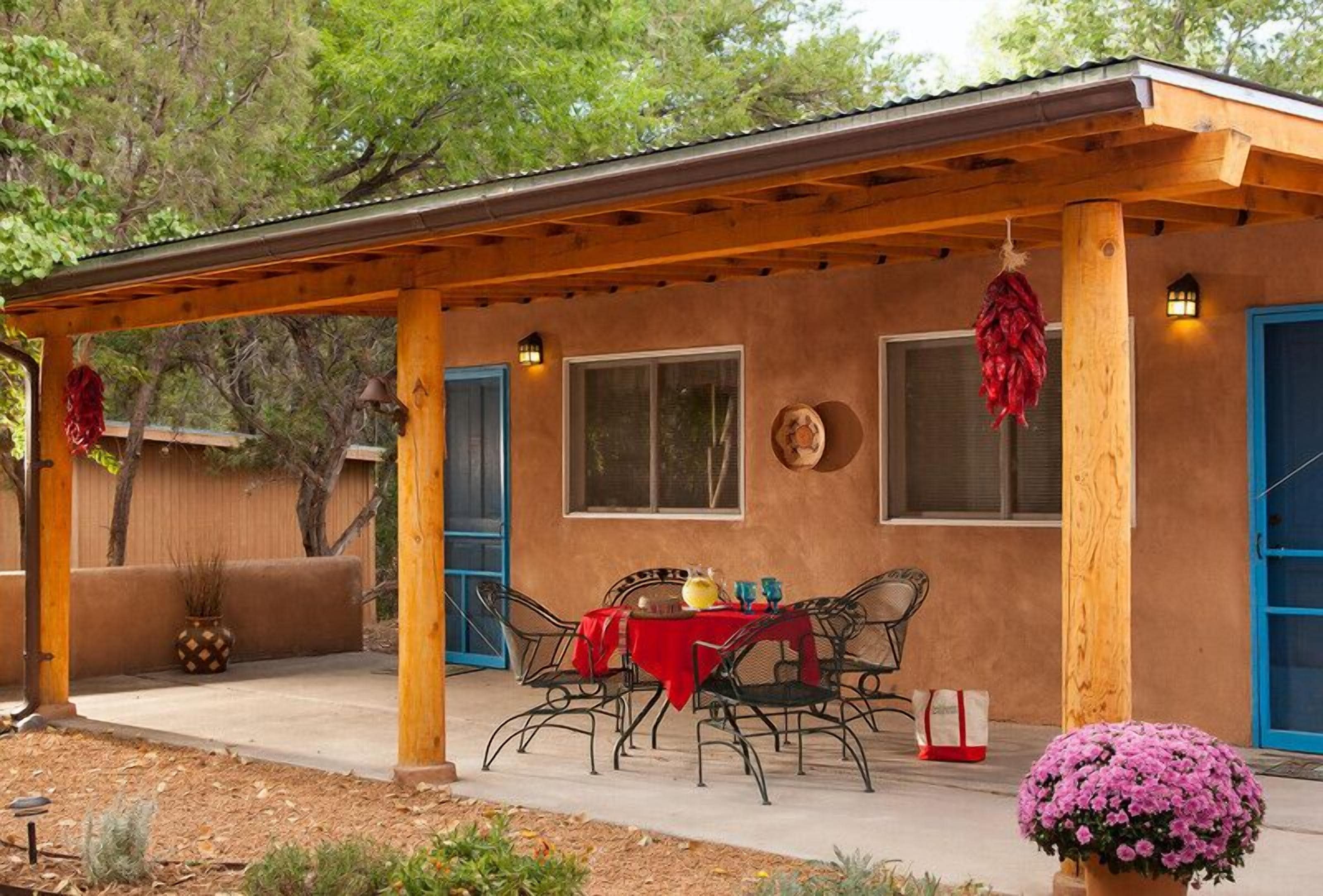 A covered patio with a table and chairs, a potted plant, and a door with a blue frame.