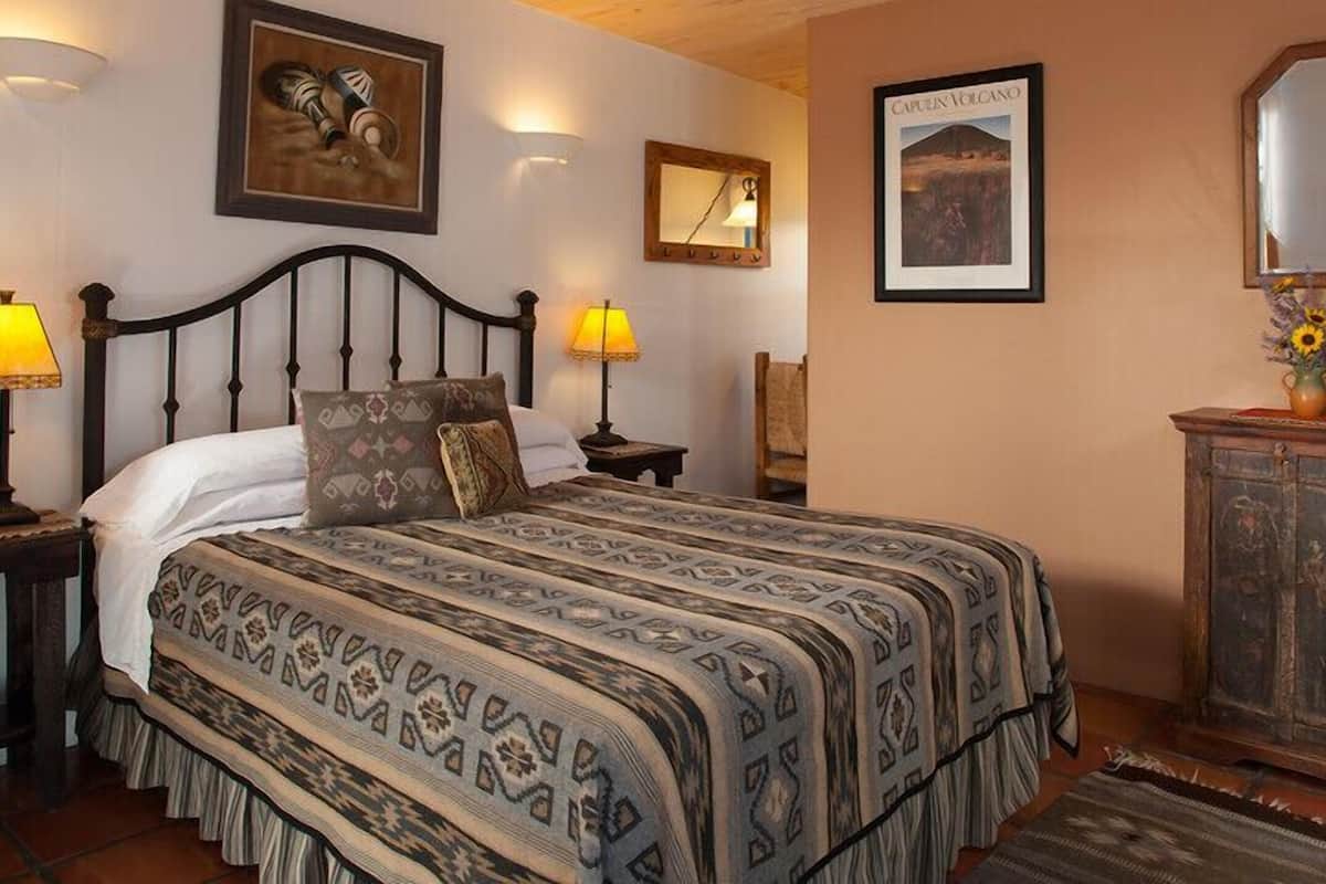 Une chambre à coucher avec un grand lit, deux lampes de chevet, une tête de lit en bois, un miroir et un tableau encadré représentant un volcan.