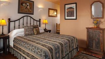 A bedroom with a large bed, two bedside lamps, a wooden headboard, a mirror, and a framed picture of a volcano.