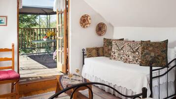 A bedroom with a bed, a chair, a table with a vase of flowers, and a view of the outdoors.