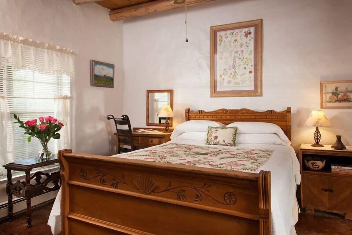 Une chambre avec un lit en bois, une table de chevet avec une lampe, une chaise et une fenêtre décorée de fleurs.