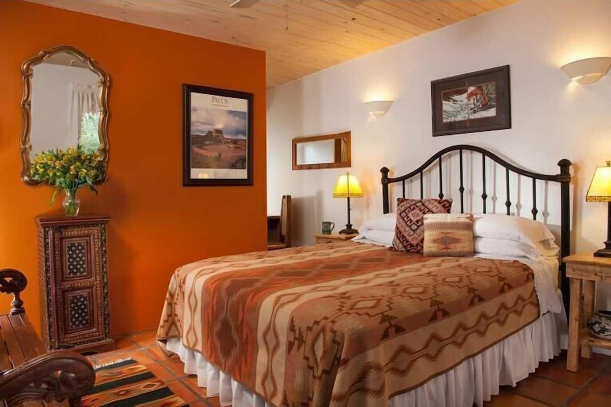 Une chambre à coucher avec un lit, une table de chevet en bois, un miroir et une lampe fixée au mur.