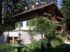 A traditional chalet with a sloped roof, a wooden staircase, and a small garden with a fountain. - Villa Stresov (Samokov)