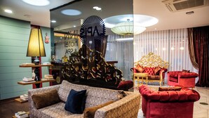 A room with a patterned sofa, a red armchair, a decorative wall piece, and a chandelier.