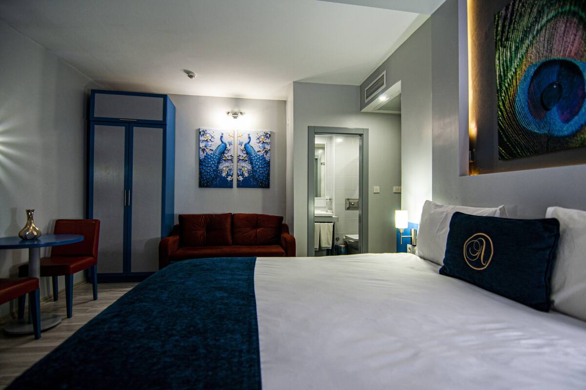 A hotel room with a large bed, a desk, a chair, a sofa, and artwork on the walls.