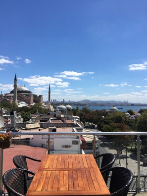 A terrace with a wooden table and wicker chairs, overlooking a cityscape with historic buildings and a river. - Lapis Inn Hotel & Spa (Istanbul)