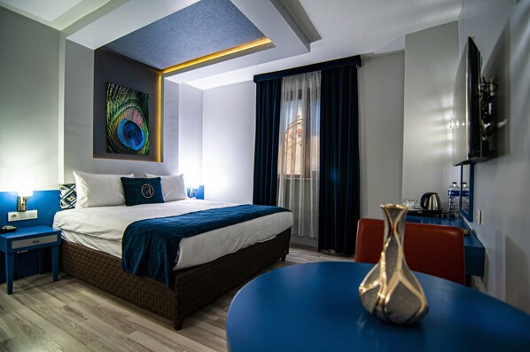 A modern hotel room with a large bed, a desk, and a dining table.