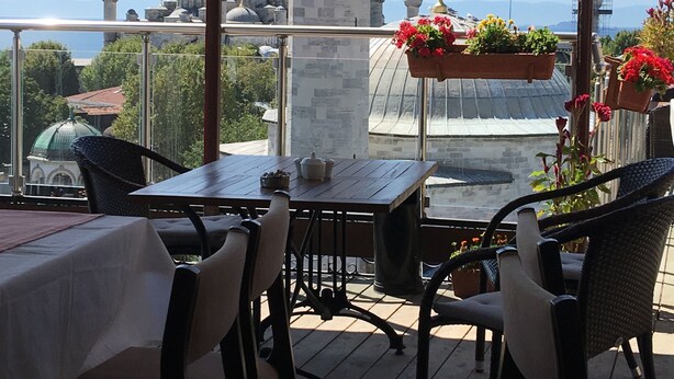 A terrace with tables and chairs overlooking a historic building with domes and minarets.