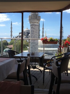 A terrace with tables and chairs overlooking a historic building with domes and minarets.