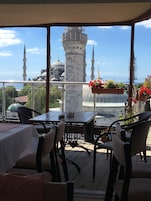 A terrace with tables and chairs overlooking a historic building with domes and minarets.