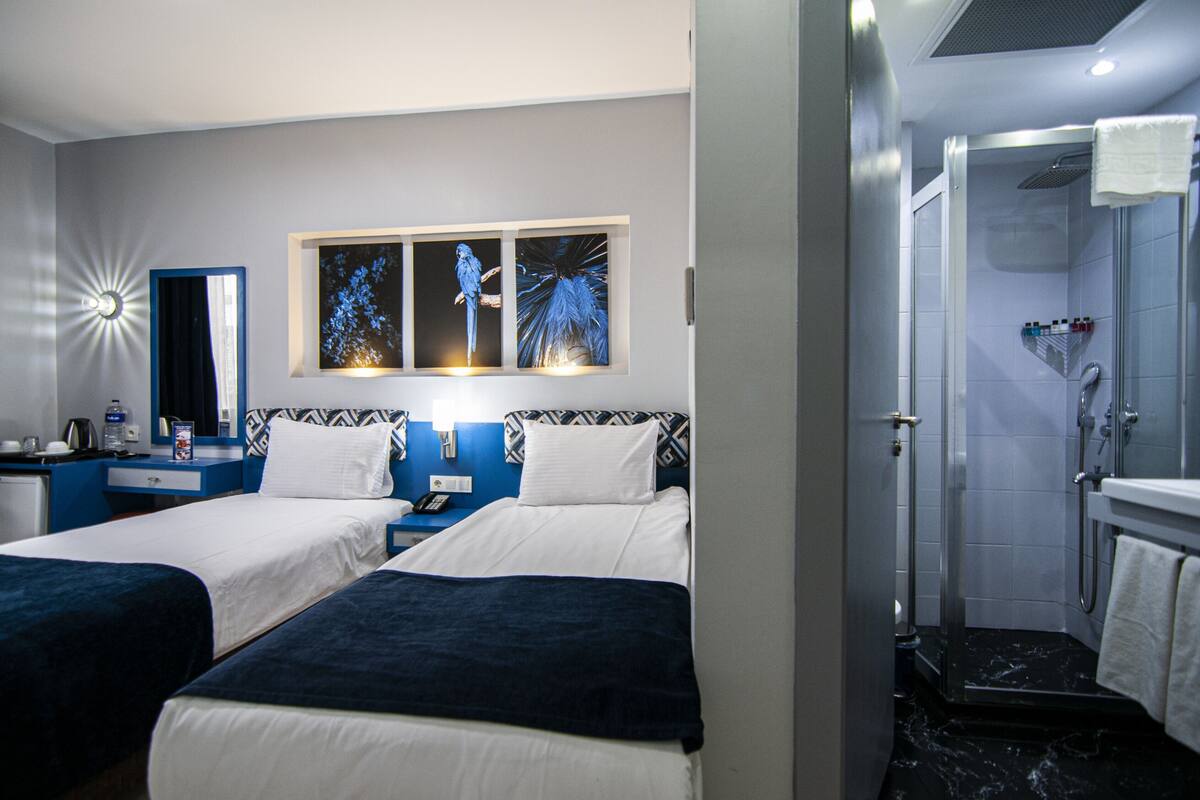 A hotel room with two beds, a nightstand, a mirror, and a wall-mounted artwork.