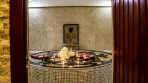 A circular hot tub with candles and towels, surrounded by a tiled wall.