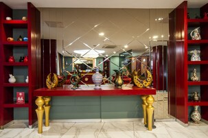 Un hall de hotel con una mesa roja central que exhibe diversos objetos decorativos, flanqueado por estanterías rojas con cristalería.