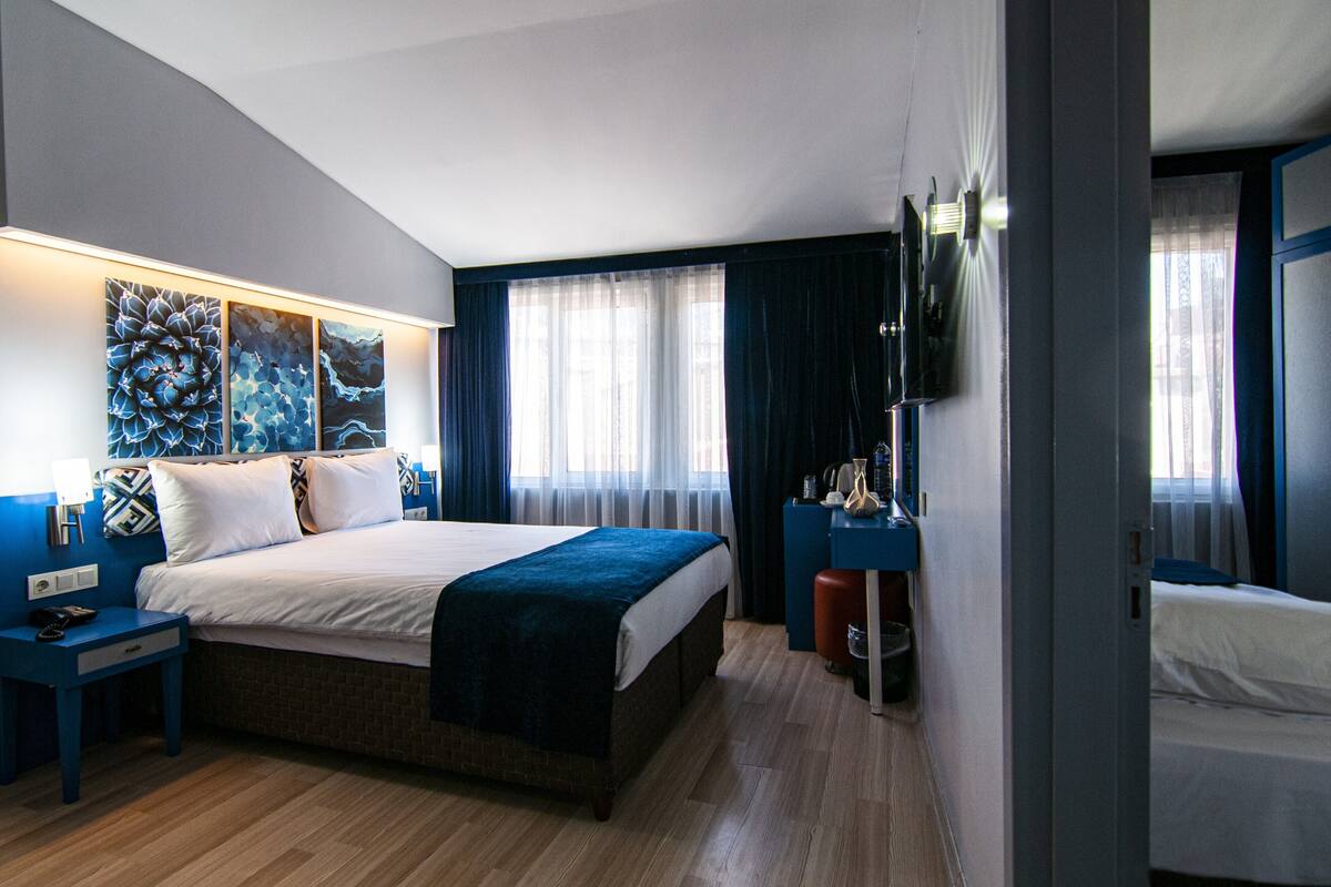 A modern hotel room with a large bed, a desk, and a flat-screen TV mounted on the wall.