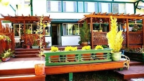 A wooden bench with potted plants in front of a building with a green door and windows.