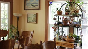 A dining area with wooden chairs, a table, and a plant shelf with various potted plants.