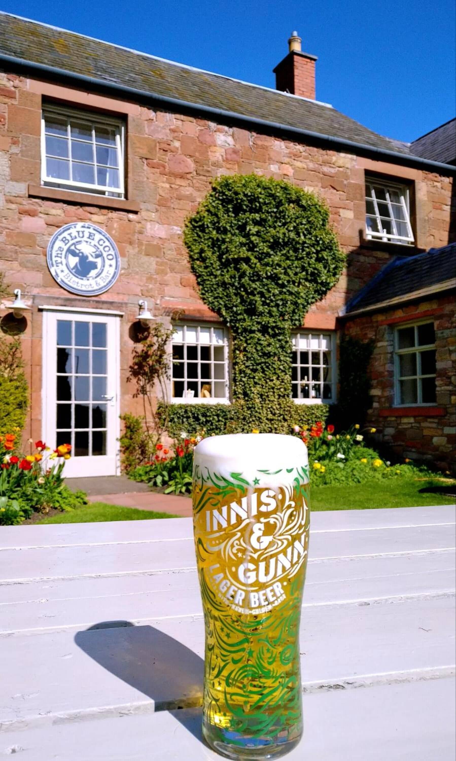 A beer glass in front of a building with a stone facade, a round window, and a sign that reads "The Blue Co."