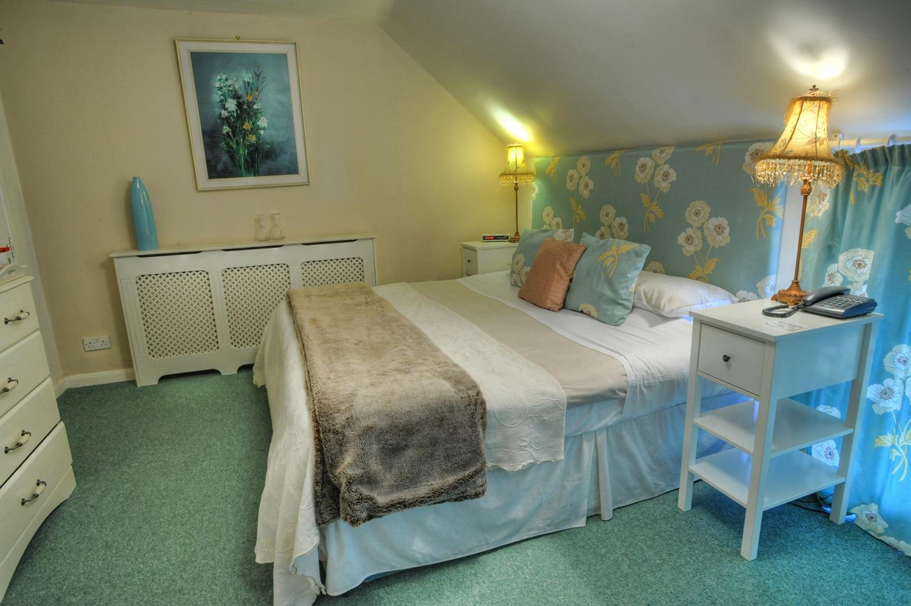 A bedroom with a bed, bedside table, lamp, and a painting on the wall.
