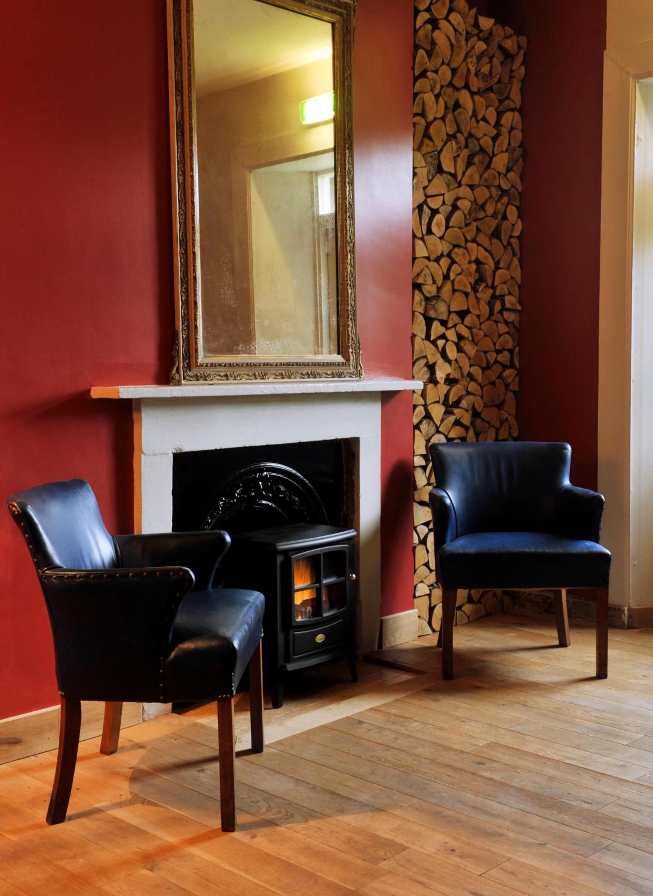 Una habitación con chimenea, dos sillones de cuero negro y un espejo grande encima.