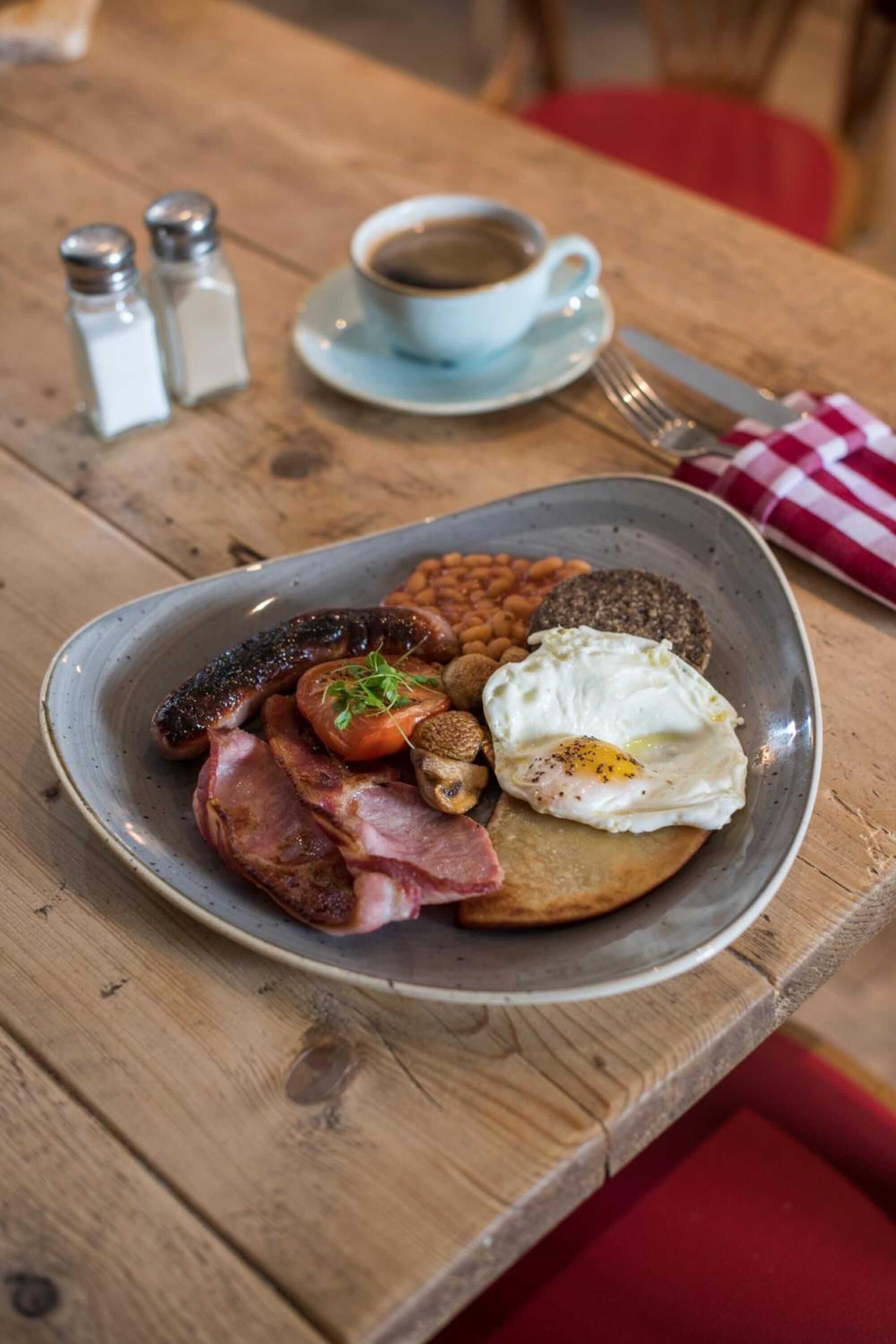 Un plato de desayuno con huevos, salchichas, tocino, champiñones y frijoles sobre una mesa de madera.