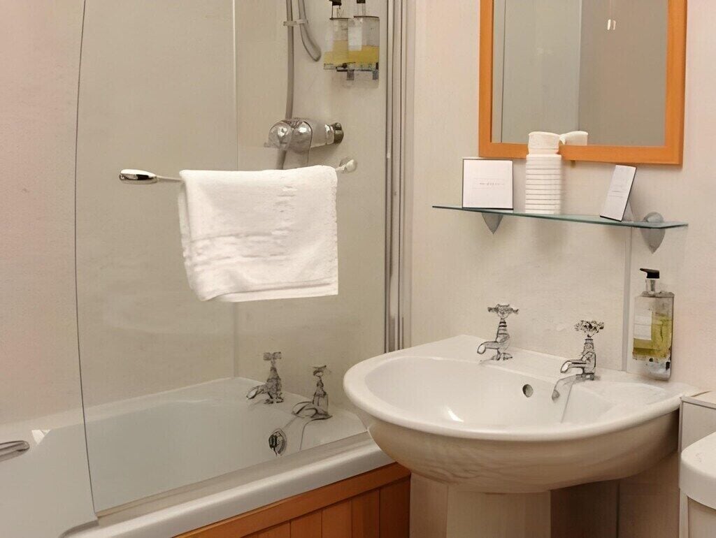 A bathroom with a glass-enclosed shower, a white sink, and a mirror with a wooden frame.