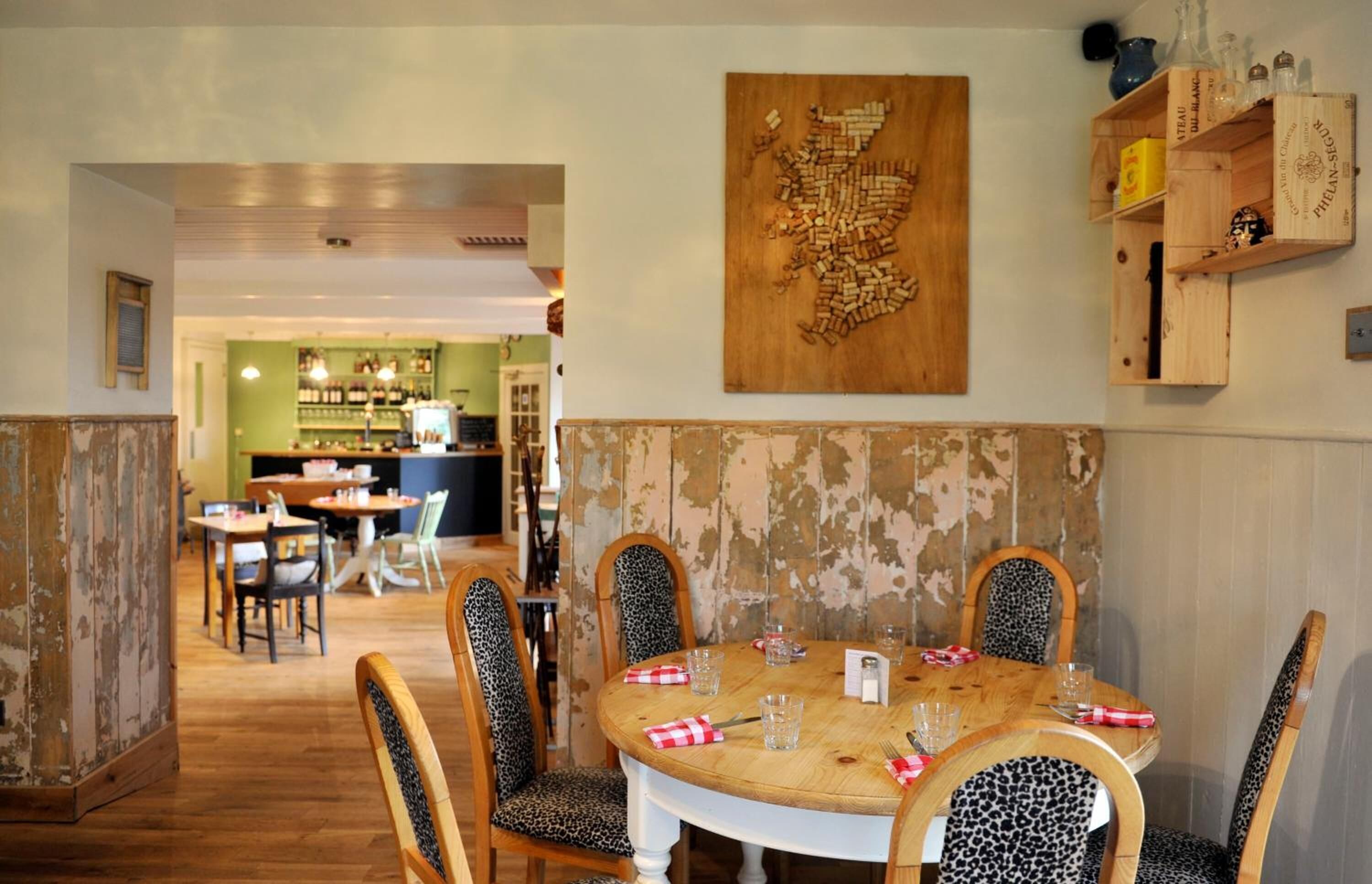Un comedor con una mesa redonda dispuesta para cuatro, sillas de estampado de leopardo y una pieza de arte de madera en la pared.
