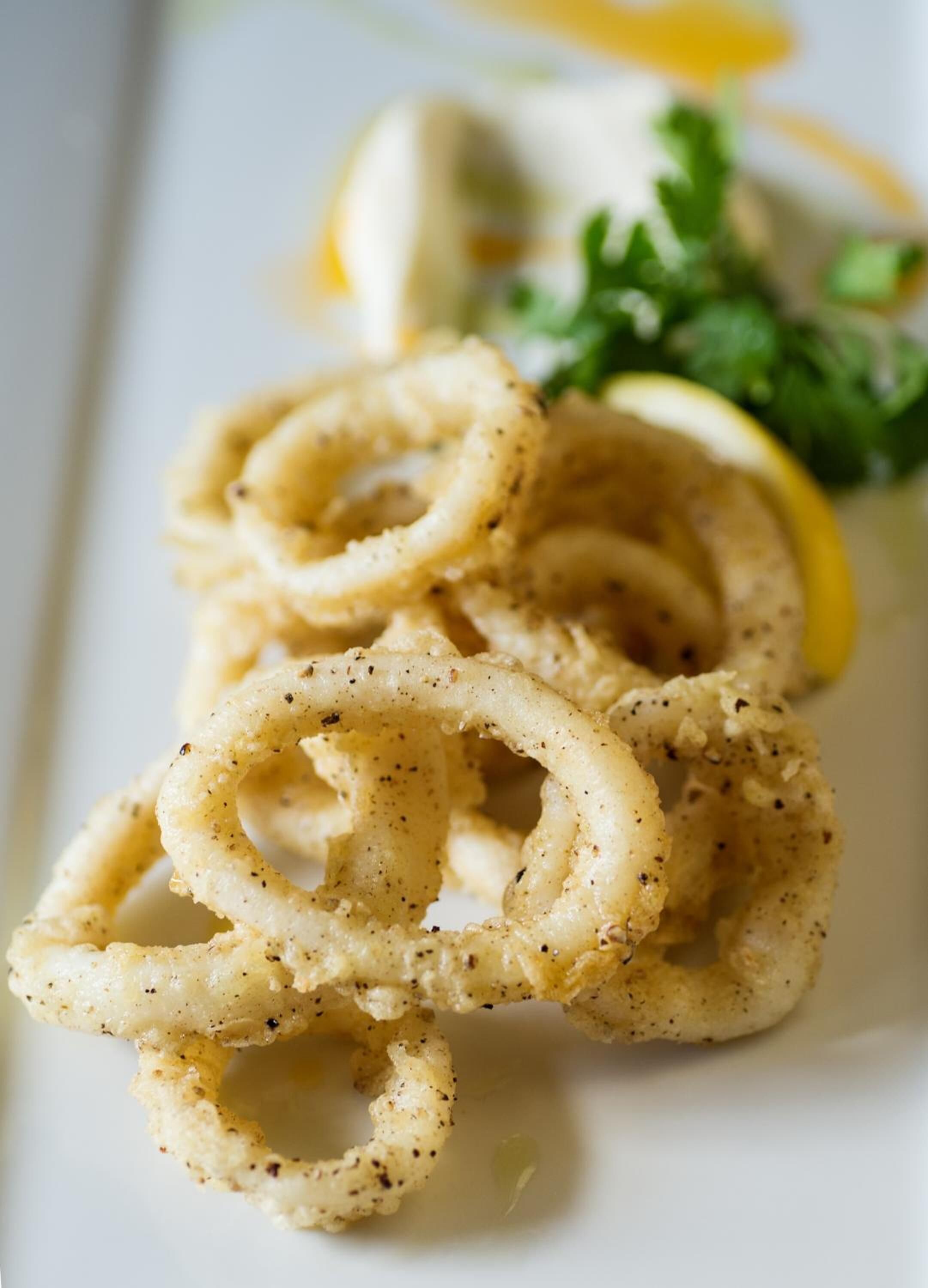 A plate of fried calamari with lemon wedges and parsley garnish.