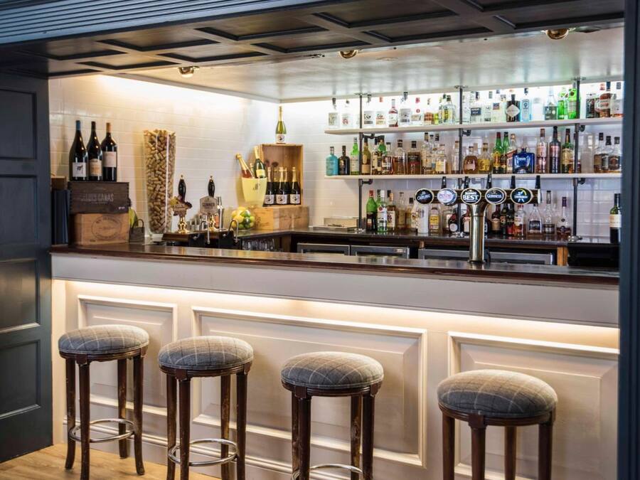Zona de bar con mostrador, taburetes y estanterías llenas de botellas.