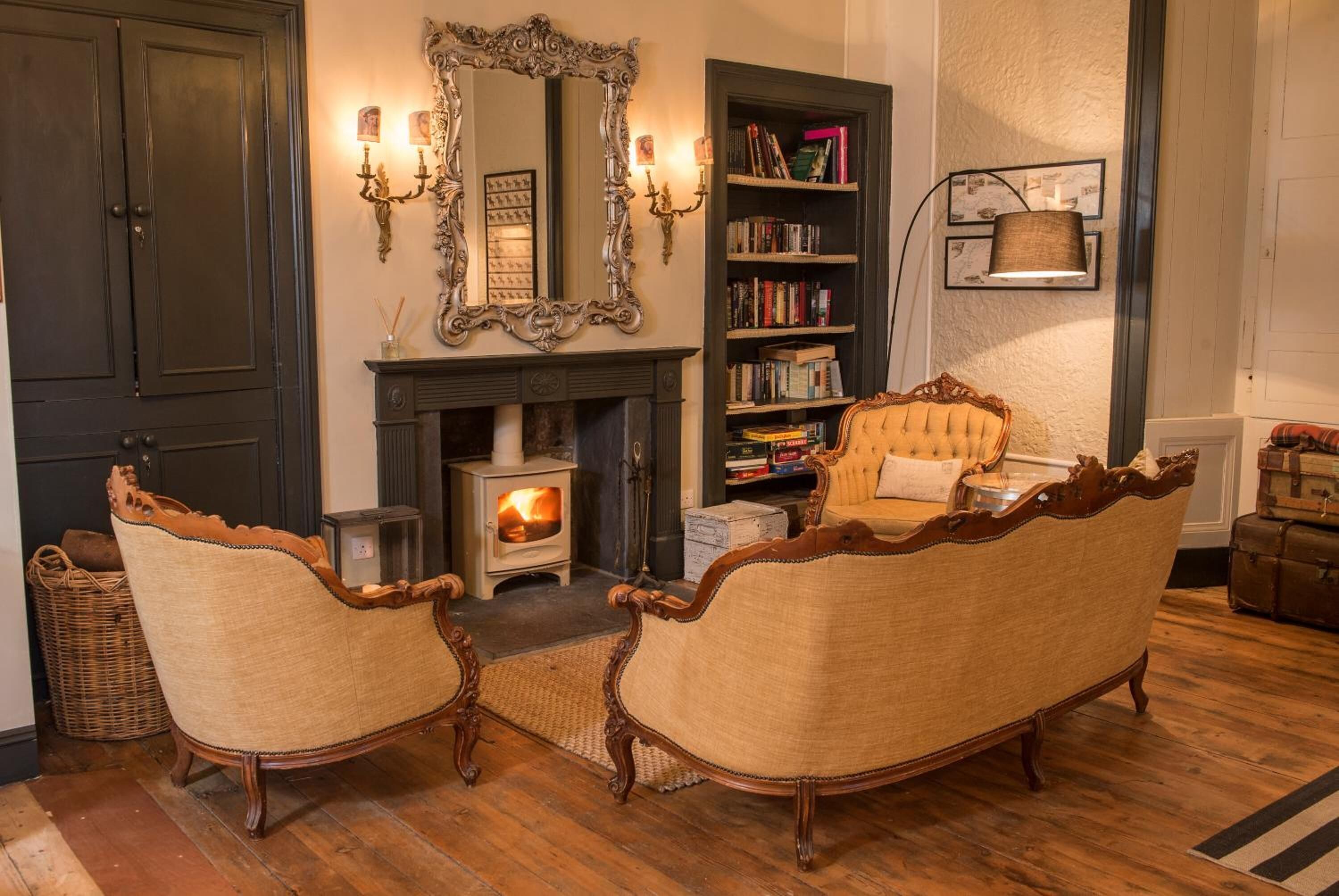 Un salon chaleureux avec une cheminée, deux fauteuils rembourrés, une bibliothèque et un grand miroir décoratif.
